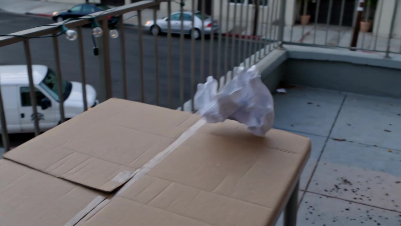 Drifting plastic bag lifting off box by breeze, rotating, settling by stacked boxes on balcony
