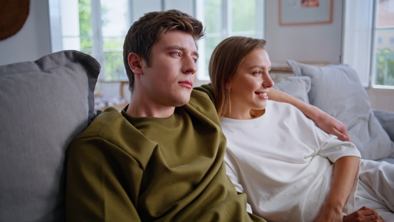 Happy lovers watching tv together on weekend. Teenager couple embracing on sofa