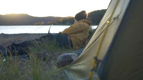 Kleiner-Hund,-Der-Auf-Dem-Campingplatz-Spielt,-Während-Der-Besitzer-In-Der-Nähe-Des-Campingzeltes-Ruht---Mittlere-Zeitlupenaufnahme