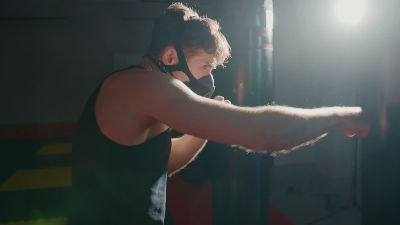 Man in Training Mask Punching Heavy Bag in Dark Gym