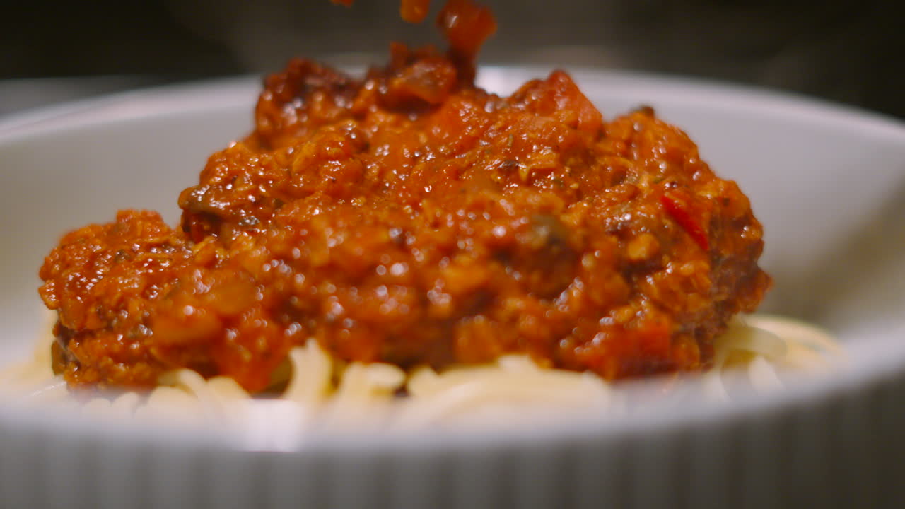 Bolognese Sauce Gently Lowered onto Spaghetti Pasta with Serving Spoon. Italian Food Traditional Classic Cuisine Made with Beef Mince and Vegetables including Mushrooms, Peppers, Onions 4K.