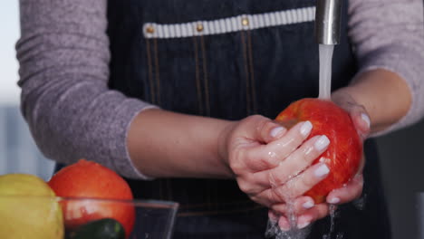a woman washes a juicy red apple under a tap