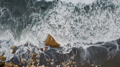 Aerial-view-upwards,-of-great-waves-of-turquoise-water-on-the-shore-with-stones-of-a-beach