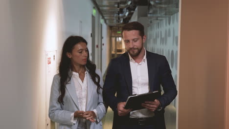 a young businessman and a young businesswoman walk through the corridors of an office building discussing company matters.