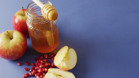 Video-of-honey-in-jar,-cranberries,-apples-and-apple-slices-lying-on-blue-surface