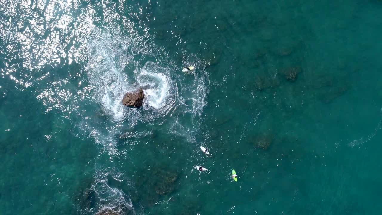 바위 근처에서 파도를 기다리는 서퍼들의 공중 드론 뷰에서 넓은 탑다운 샷