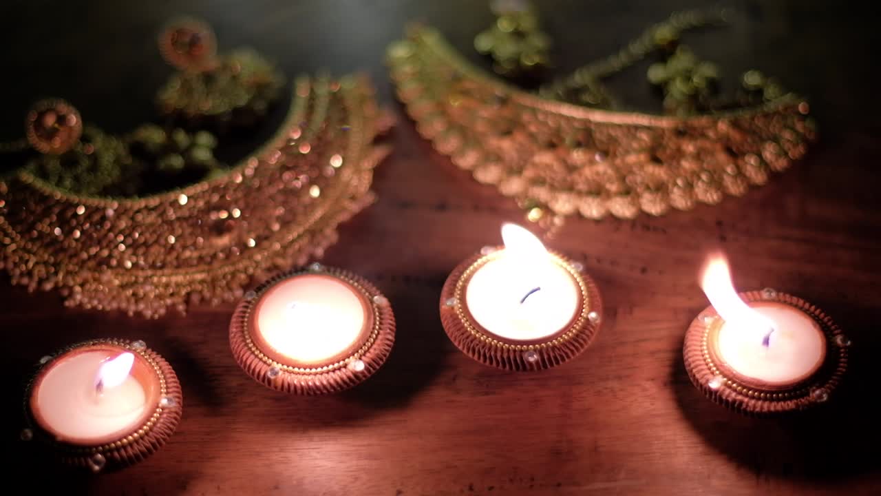 Close-up tilt down to wax diya candles burning shadow with golden jewellery for worship of wealth, prosperity and Laxmi during the Hindu festival of lights or Diwali.
