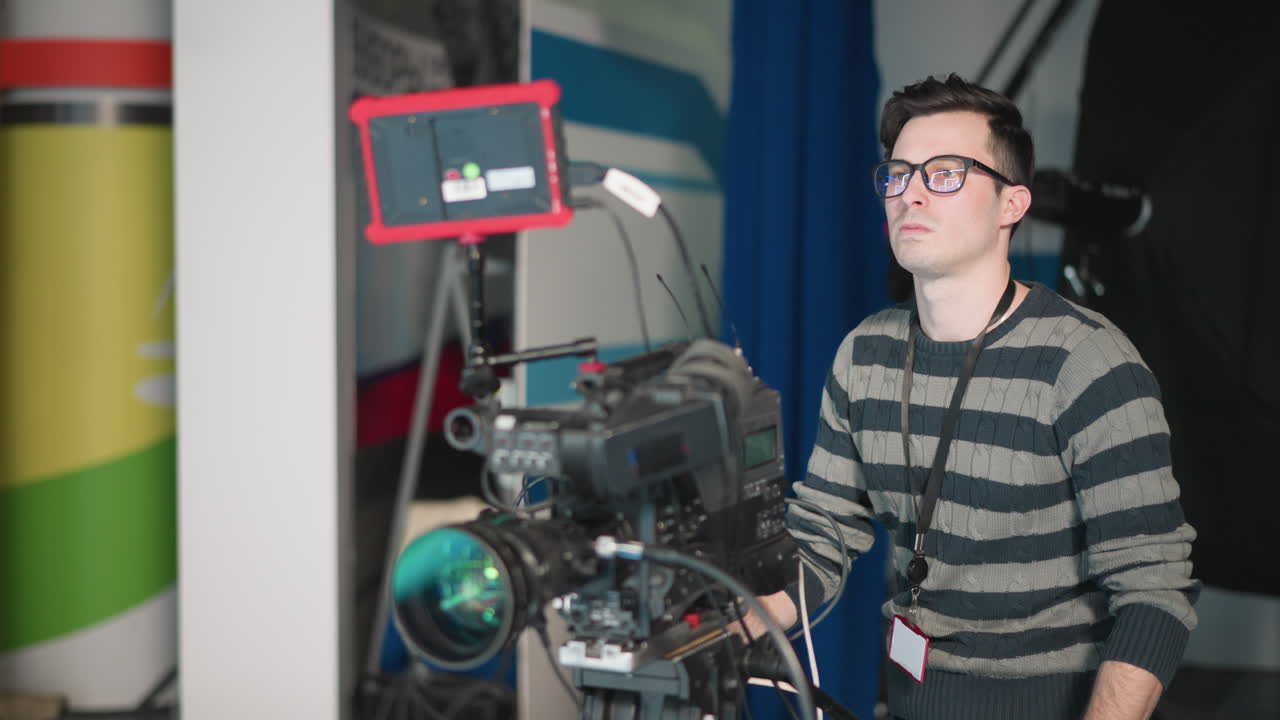 Camera operator focused on adjusting broadcast camera settings. Professional filming setup with monitor and equipment in modern television studio environment