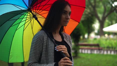 Retrato-De-Una-Joven-Hermosa-Mujer-Caminando-Con-Un-Paraguas-Colorido-En-Un-Día-Lluvioso-En-El-Parque-De-La-Ciudad