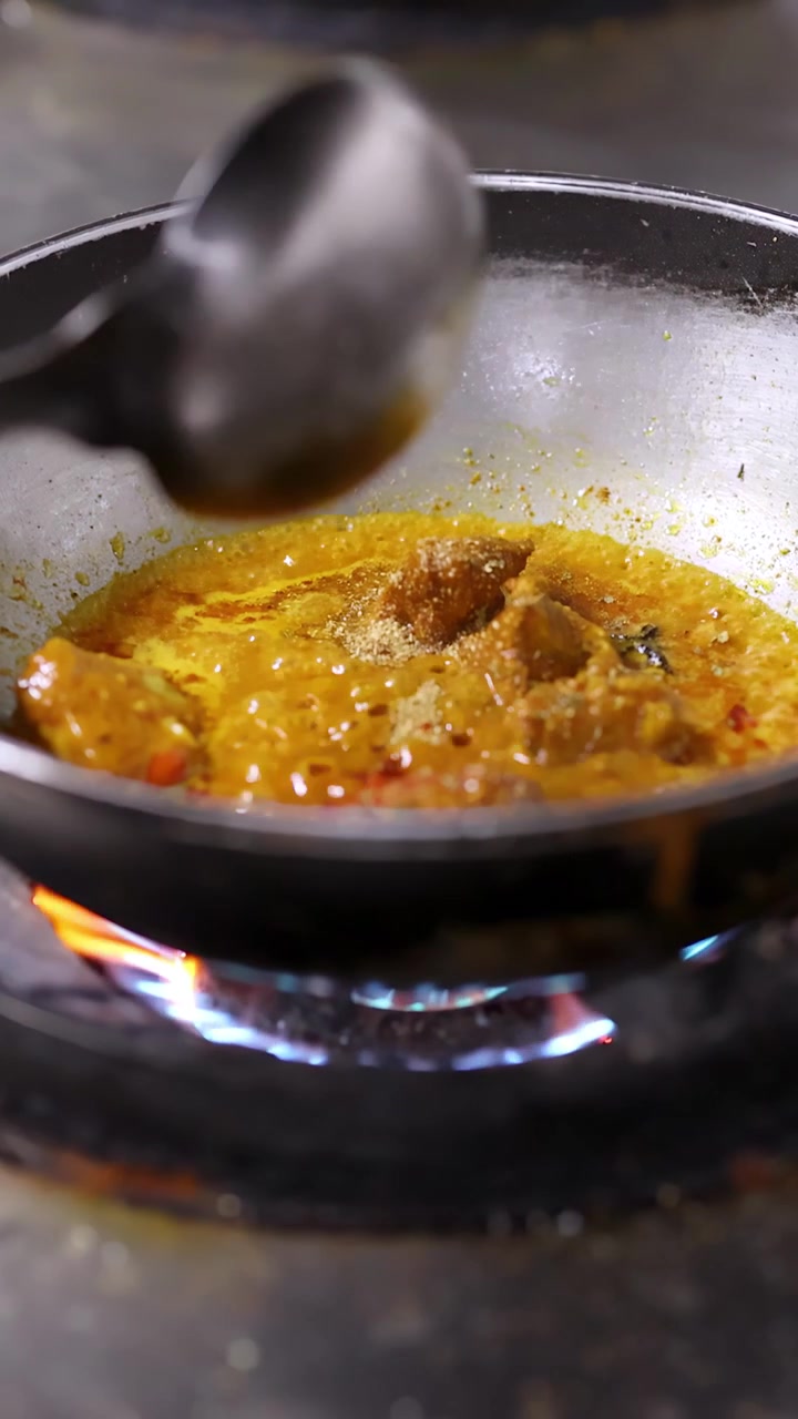 Primo piano di curry giallo che sobbolle su un fornello a gas in una cucina professionale.