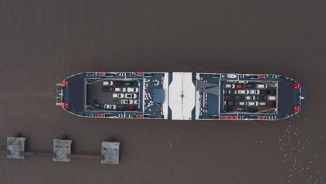 Overhead-top-down-aerial-drone-shot-of-car-ferry-leaving-docks-fully-loaded-seagulls-swarming