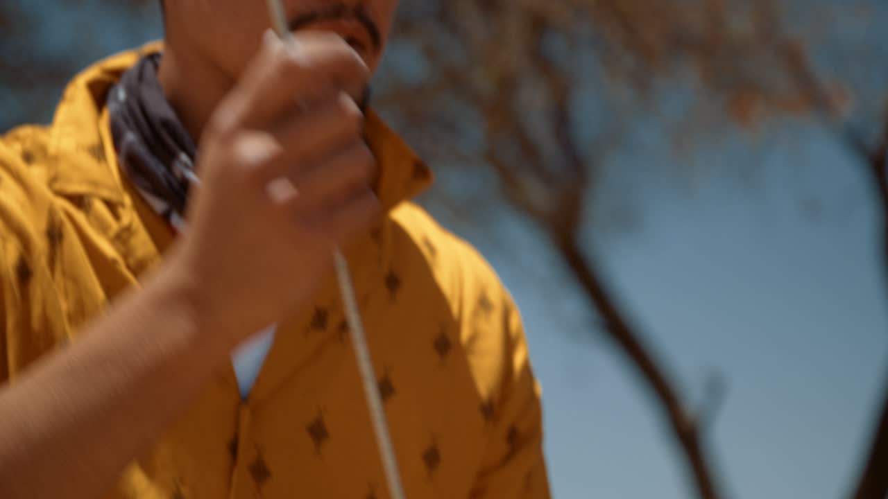 Hand held tracking shot of a off-roading Caucasian male tourist in Africa as he pulls out a tent peg from a bag and walks towards a canvas rooftop tent.