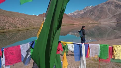 sideways moving shot of a huge himalayan lake with prayer flags at chadratal lake , spiti valley