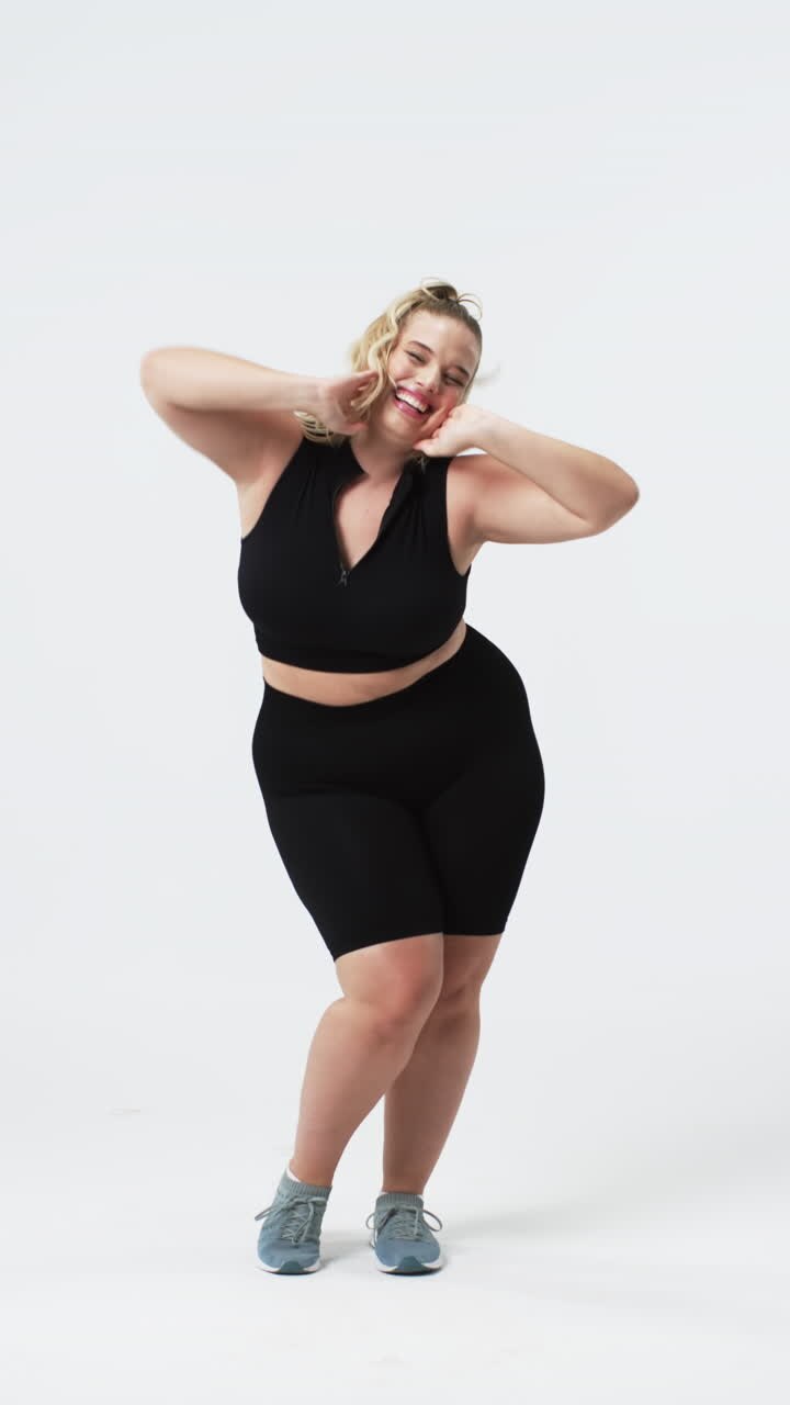 Vertical video: Dancing joyfully, plus size woman in athletic wear celebrating body positivity