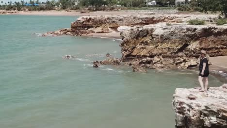 Woman-standing-on-cliff-face-admiring-blue-ocean-water