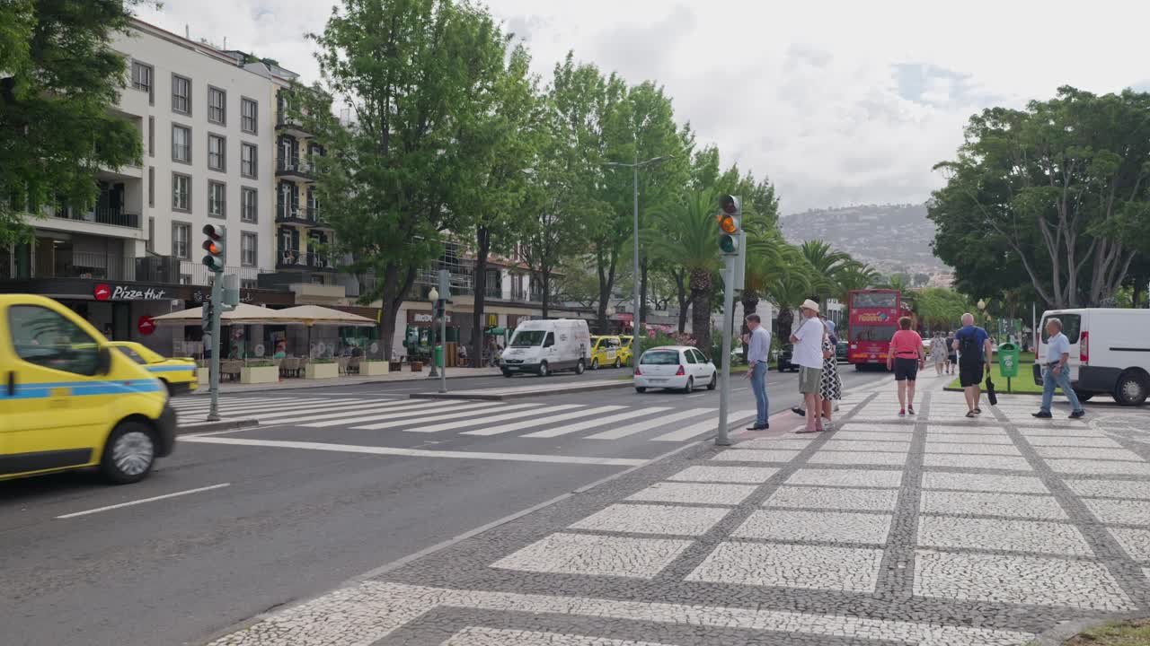 Traffic light change to red and pedestrians cross street at Funchal city
