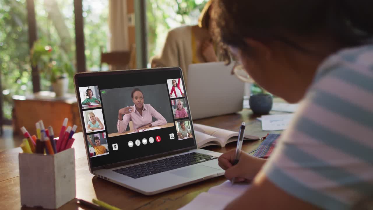 Girl doing homework and having a video conference with teacher and classmates on laptop at home