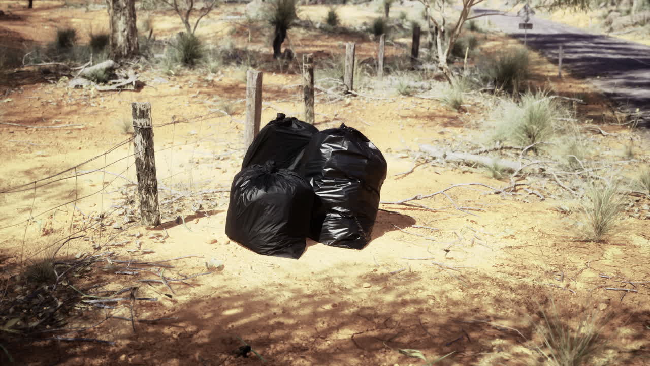 Trash bags left on the ground in a rural area surrounded by nature