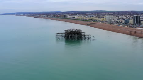 una toma aérea sobrevolando la ruina del muelle oeste en brighton en la costa costa de inglaterra con gaviotas volando alrededor