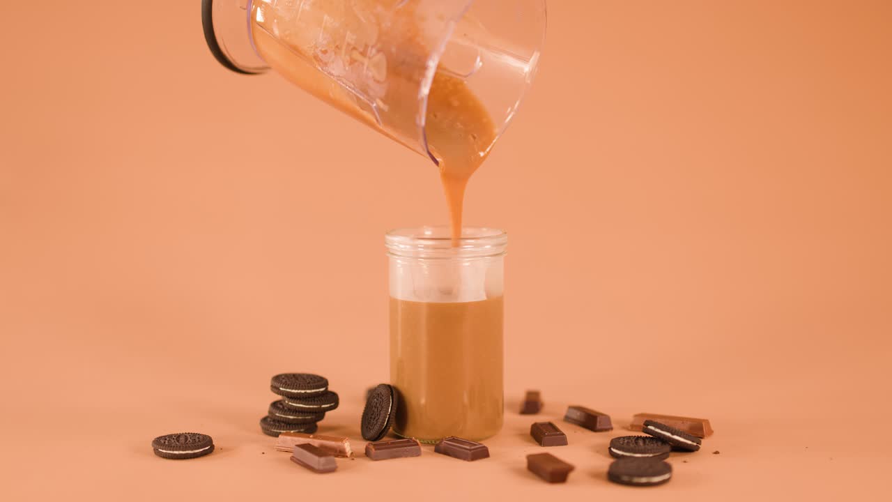 Blender pours creamy chocolate drink into glass jar, surrounded by cookies and chocolate bars