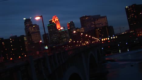 Plano-Medio-Ancho-De-Tráfico-Nocturno-Sobre-El-Río-Mississippi-Con-El-Horizonte-De-Minneapolis,-Minnesota