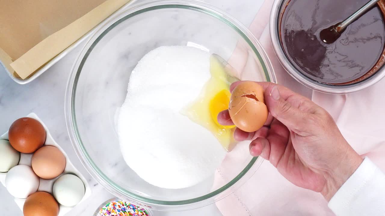 Chocoladebrownies bakken en eieren breken om aan het beslag toe te voegen. Brownies maken op een witte achtergrond, omringd door eieren, een roze servet en een bakvorm. In de keuken een chocoladedessert maken