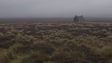 heather and grass covering moorland terrain, with fog partially shrouding a lonely house in the distance on a cloudy day, creating an atmospheric and tranquil scene