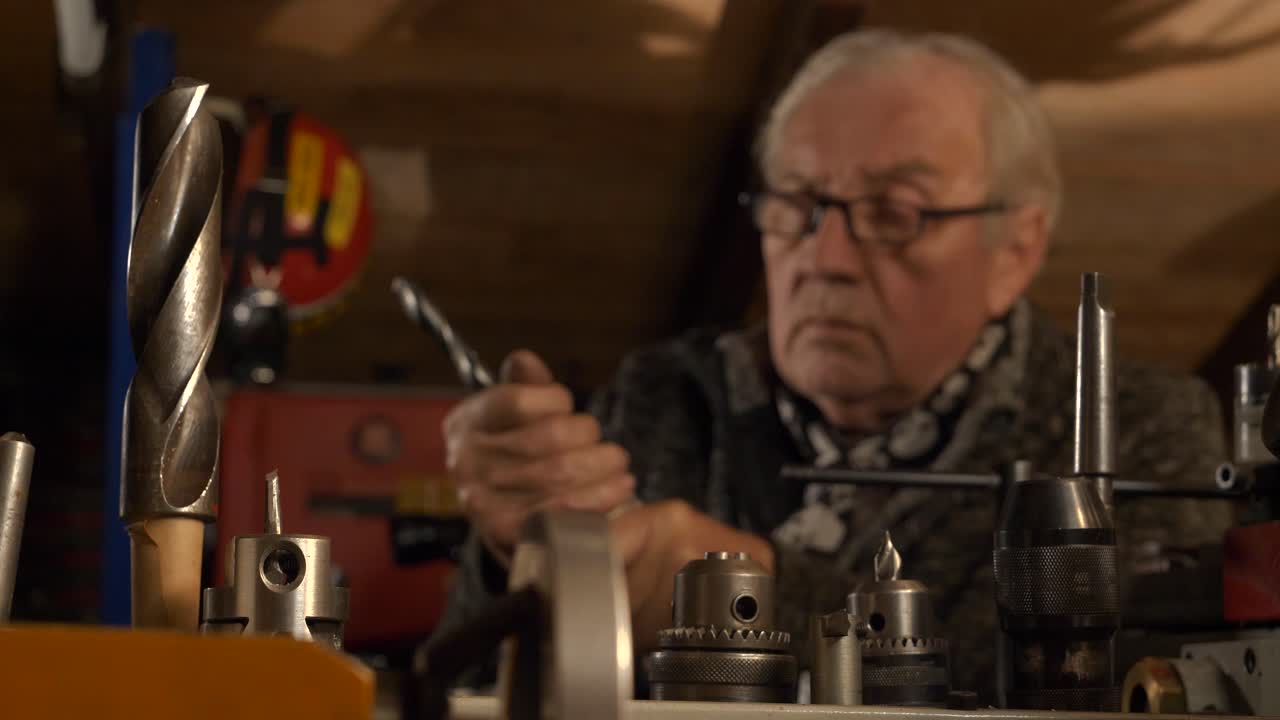 trabajador sénior que maneja piezas de máquinas de perforación en un taller, centrarse en piezas de perforacion