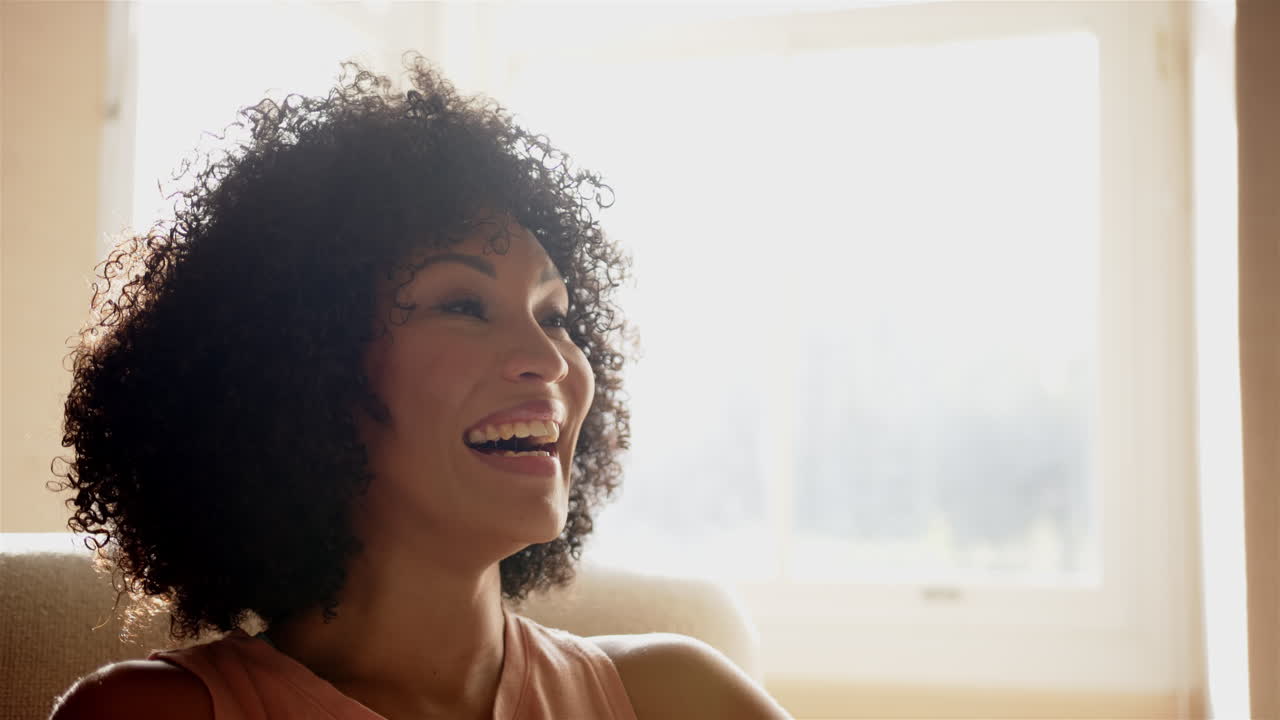 Smiling woman with curly hair sitting on chair, enjoying bright sunlight, copy space