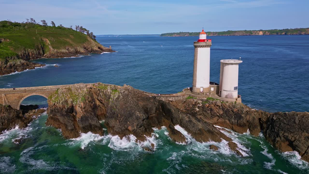 Orbital drone shot from left to right around Petit Minou lighthouse, showing the side path, crashing waves, and rocky cliffs. Brittany in France