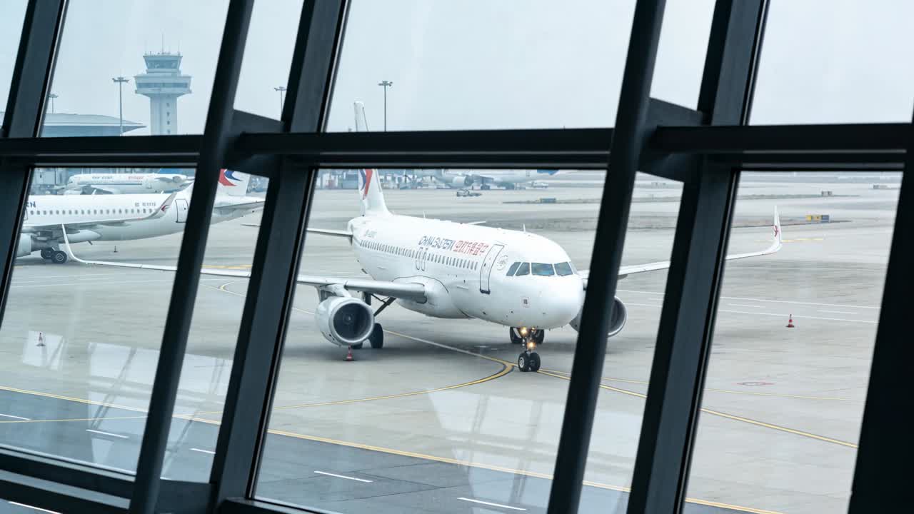 Jet a corridoio singolo in rullaggio verso il terminal dopo l'autorizzazione della torre, attraverso finestre inclinate, su piazzale bagnato.