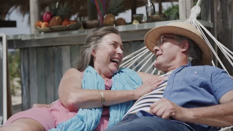 una feliz pareja caucásica anciana acostada en una hamaca riendo fuera del bar de la playa, en cámara lenta.