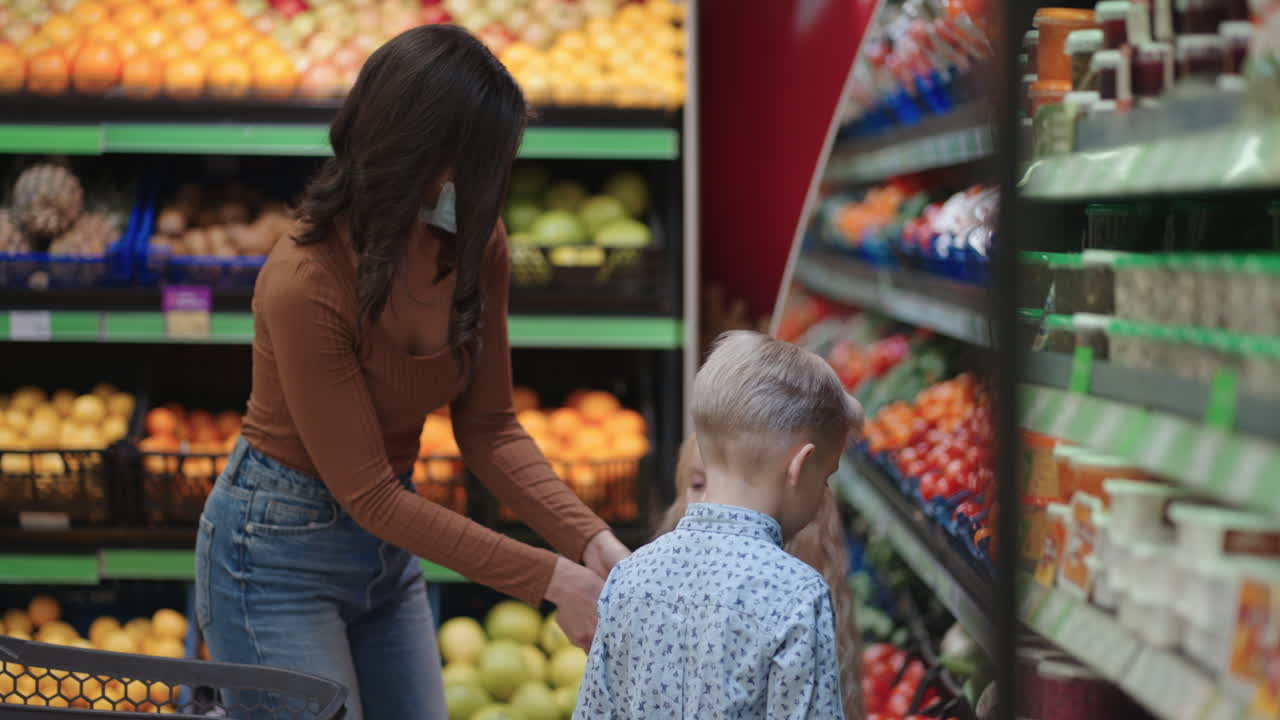 una madre con una máscara protectora con dos hijos está comprando comestibles en el supermercado. comprando alimentos, verduras y frutas con niños