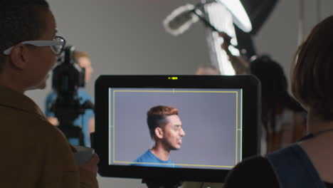 female director and film crew watching male actor shooting movie or video in studio on monitor 1