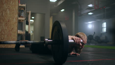 a man pushes up by rolling a barbell with one hand on the floor of the gym in slow motion