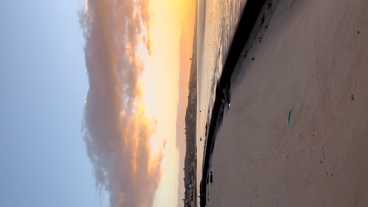 Vertical romantic view of a calm beach at sunset. The sea with houses in the background