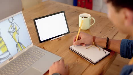 Diseñador-De-Moda-Masculina-Birracial-Dibujando-Diseño-En-El-Escritorio-Usando-Una-Computadora-Portátil-Con-Espacio-Para-Copiar,-Cámara-Lenta