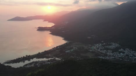 paralaje aéreo de la bahía de la playa de pui o y el mar junto al pueblo rodeado de colinas de la selva tropical a la hora dorada, la isla de lantau, hong kong, china