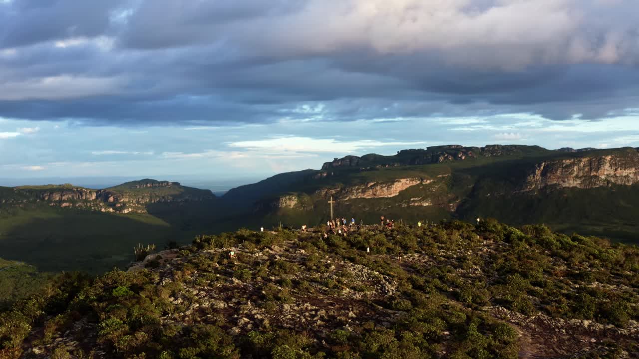 dolly out volando un paisaje de drones tomado de la cima del morro do pai inacio en el parque nacional chapada diamantina en el norte de brasil con excursionistas rodeando una cruz gigante en una cálida y soleada tarde de verano