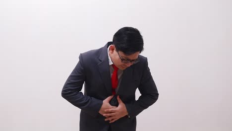 asian businessman in suit suffering from stomach ache, hands holding stomach