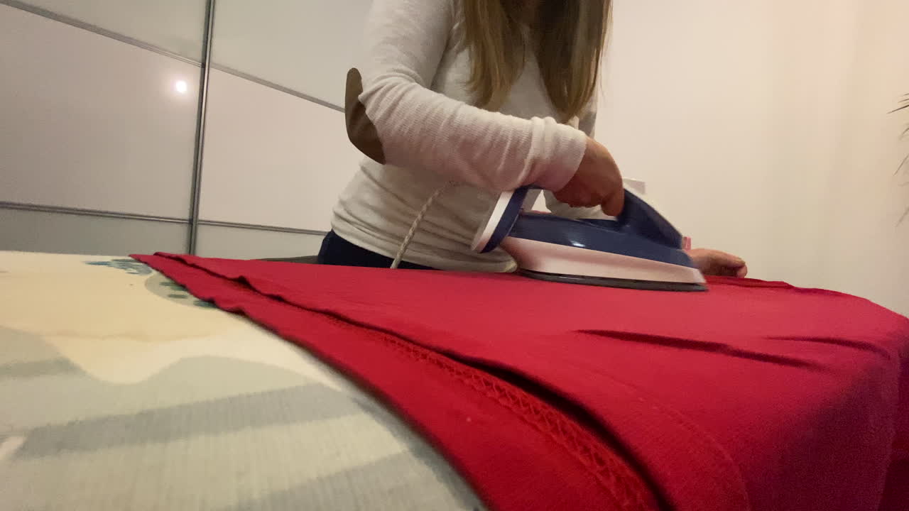 La donna stira una camicetta rossa su un asse da stiro