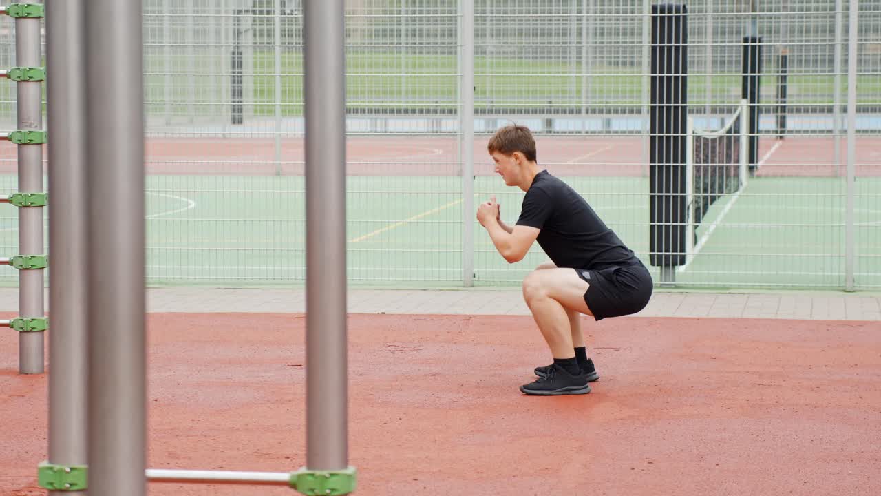 A young man performs squats in an outdoor sports park, focusing on strength and fitness training