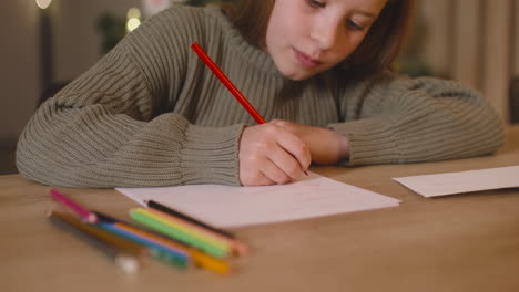 Vista-De-Cerca-De-Una-Chica-Con-Suéter-Verde-Escribiendo-Una-Carta-Y-Pensando-En-Deseos-Sentada-En-Una-Mesa-En-Una-Habitación-Decorada-Con-Un-árbol-De-Navidad