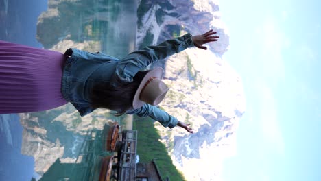 woman with a hat raising her arms in front of croda del becco in dolomites