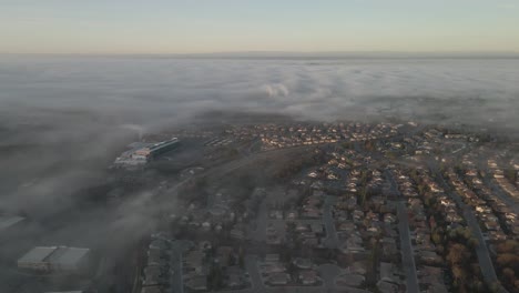 Dreamy-drone-wideangle-footage-over-Folsom,-USA-showing-houses-and-streets-through-the-low-lying-misty-clouds,-and-pastel-coloured-mountains-in-the-distance