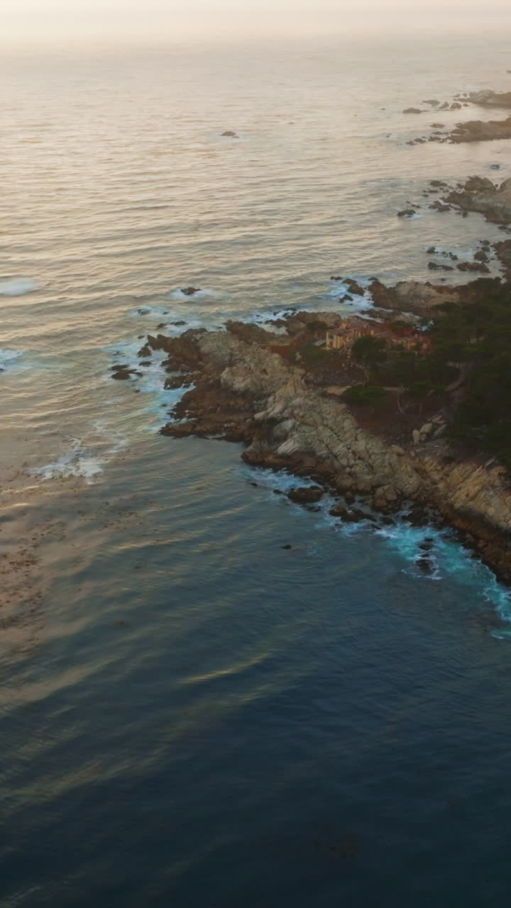 Rocky shore of Pacific Ocean with some houses in Carmel-by-the-Sea. Lots of green trees growing on the craggy coastline. Sunset background. Vertical video