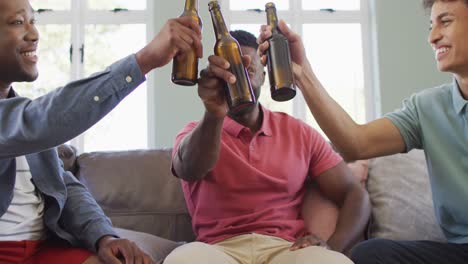 happy diverse male friends talking and drinking beer in living room