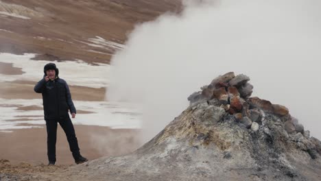 tourist stand near active rocky steam vent and point direction, iceland