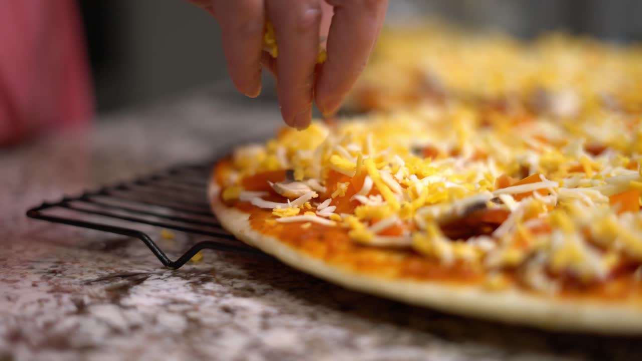 Chef at home putting mozzarella and cheddar cheese onto pizza close up. Female cook applying fresh ingredients while making Italian pizza. Close-up on hands putting cheese on thin crust pizza uncooked