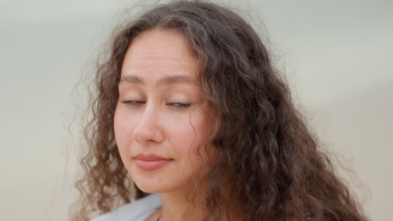Island beach portrait contemplative woman gazing, soft curly hair, warm sunlight, gentle breeze, calm waves, candid expression, relaxed posture, seaside horizon, natural skin texture, subtle smile